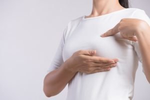Mulher apontando para o seio - câncer de mama
